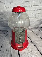 Full view of the red metal gumball machine with clear globe and detailed coin slot mechanism.