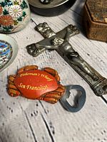 Close-up photo of crab-shaped bottle opener and metal crucifix, showing details and condition.