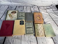 Photo showing 9 vintage and antique books arranged on floor, showcasing variety in size, color, and condition of covers.
