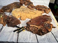 Multiple irregularly shaped redwood burl wood pieces laid out on a wooden surface, showing natural grain and textures, plus small cylindrical attachments.