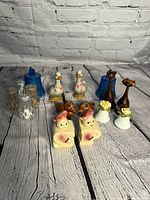Photo showing all 9 vintage salt and pepper shakers arranged on a white wood plank surface with a grey brick wall background.