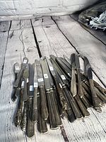 Photo showing various silver plated cutting utensils laid out on wooden surface, including multiple knives with detailed handles.