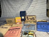 Vintage puzzles, a metal bank, playing cards, and craft box arranged on a wooden surface in front of a white brick wall background.
