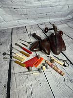 Photo showing the entire lot including wooden shoe lasts, rotary cutters, scissors, sewing thread, pipe, and shoemaker's wax, arranged on a rustic white wooden surface.