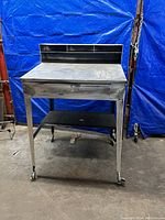 Front view of vintage metal warehouse desk showing drawer and casters