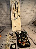 Full view of assorted jewelry including beaded necklaces hanging and brooches/earrings displayed on black velvet hand form and on the table