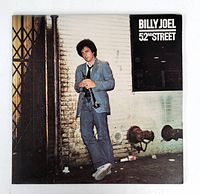 Front cover of Billy Joel's 52nd Street album featuring artist holding a trumpet by a brick wall.