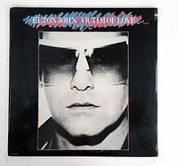 Front cover of Elton John Victim of Love LP showing black and white close-up photo and album title.