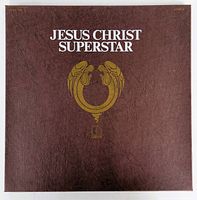 Front cover of the Jesus Christ Superstar album box showing brown textured cover with white title and gold emblem design.
