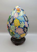 Full view of the cloisonne egg on the wooden stand showing multicolored flower patterned enamel work on blue background.