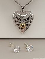 Front view of heart-shaped sterling silver locket necklace with gold-plated heart detail on chain, and pair of cubic zirconia stud earrings