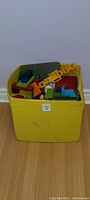Yellow box filled with assorted Duplo blocks and pieces, showing crane and building baseplates.