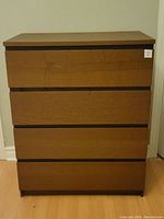 Front view of brown wooden dresser with four drawers, showing smooth panel fronts and slight marks.