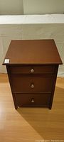Front view of the unopened brown walnut wood 3-drawer file cabinet showing metal knob handles.
