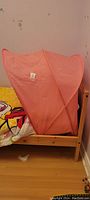 Pink child's bed canopy fully installed on a single wooden bed, showing side view with frame shape in place.