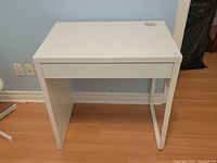 Front view of child's white study desk, showing clean flat top, metal frame leg on one side, and solid panel on the other side.