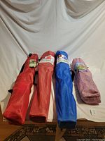 Four folded camping chairs in carrying bags: three full-size in red, maroon, blue, and one child-size in pink with star pattern