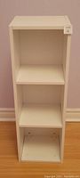 Front view of the small white standing shelf showing three compartments and overall condition.
