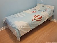 Twin bed fully made with balloon patterned fitted sheet and pillow case, white bed frame and mattress visible