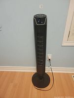 Full view of a tall black vertical oscillating tower fan standing on a round base with power cord visible.