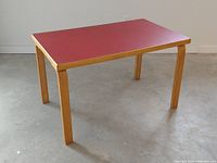 Front three-quarter view of table showing birch legs and red laminate top