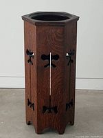 Full view of the octagonal topped wooden umbrella stand showing the dark quartersawn oak surfaces and butterfly cutout designs on sides.