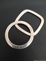 Two sterling silver bangles, one round and one square, overlapping on black background.