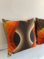 Close-up of one cushion showing vibrant op-art curved stripes in orange, yellow, brown, cream, and black textured fabric.