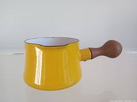 Side view of yellow enamel sauce pot with rounded teak handle