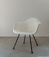 Front angle view of white fiberglass arm shell chair on black steel X base, showing clean curved shell and base condition.