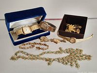 Overview of six watches displayed in a blue velvet box and on table alongside chain necklace and bracelet