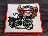 Full front view of square mirror showing Harley-Davidson Sportster motorcycle and eagle logo with red border on mirror surface.