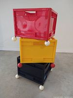 Three crates stacked vertically (red atop yellow atop black), showing ball caster wheel detail