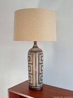 Full view of the vintage ceramic table lamp with geometric pattern and beige fabric drum shade on teak surface.