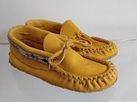 Side angle photo showing moccasin shape, yellow moose hide material, whip stitched toe, and beaded trim detail.