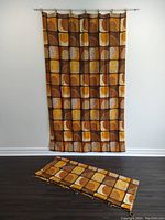 Full view of one hanging curtain panel and one folded on floor showing full pattern and metal rings