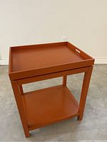 Front angle view showing the orange side table with removable serving tray on top and lower shelf.