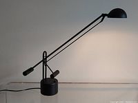 Side view displaying the full length and balanced arm mechanism of the black architect desk lamp on a transparent surface.