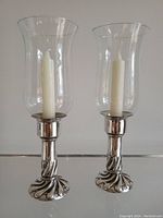 Pair of tall hurricane candle holders showing original clear glass chimneys and twisted sterling silver bases with candles inside.