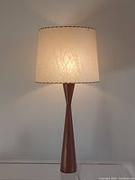 Frontal view of lit lamp showing fiberglass shade and teak base