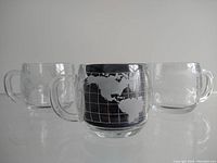 Front view showing three glass mugs with etched world maps including North and South America