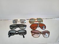 Six pairs of vintage sunglasses on a white surface showing front view and varying styles.