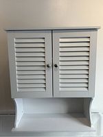 Front view showing the two louvered doors with metal knobs and the open bottom shelf.