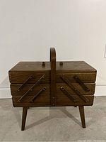 Closed view of brown vintage wooden sewing caddy with handle and fold-out compartments, standing on legs.