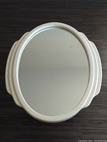 Full oval mirror with white glossy lacquer frame placed on a dark wood floor, showing overall shape and condition.