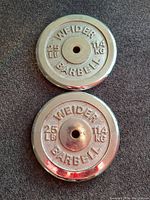 Top view of two chrome Weider barbell plates showing the embossed 25 lb and 11.4 kg markings with minor surface rust.