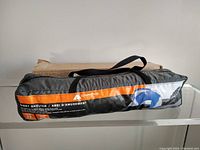 Photo of the compact carry bag with shoulder strap, showing Ozark Trail branding in orange and black with an image of the shelter.