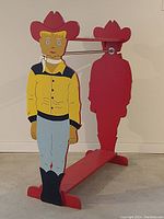 Front view of the folk art wooden cowboy figure with painted yellow shirt, red hat, and blue pants