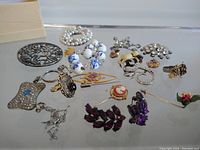 Overview of vintage women's rhinestone jewelry with brooches, rings, bracelets, and earrings spread on a reflective surface.