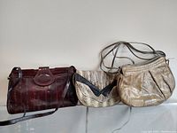 Photo of three exotic leather handbags showing different textures and colors: dark brown eel leather, light tan snakeskin, and tan/black snakeskin.